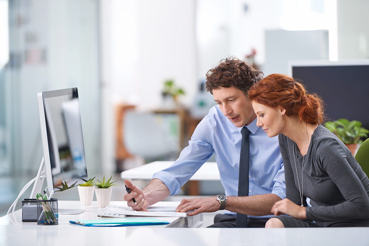 Two people have a conversation behind a desk.
